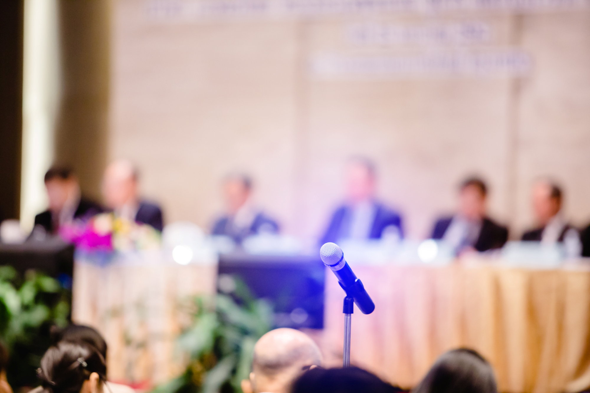 Blurry of microphone with chairman of the meeting and executive committee background in auditorium for shareholders meeting or seminar event, Annual shareholder meeting